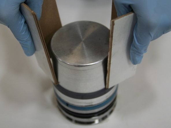 Slide the cap seal onto the piston assembly tool and push the cap seal down (using rigid cardboard) past the  modified wear ring and over the T-seal to place in the middle groove.