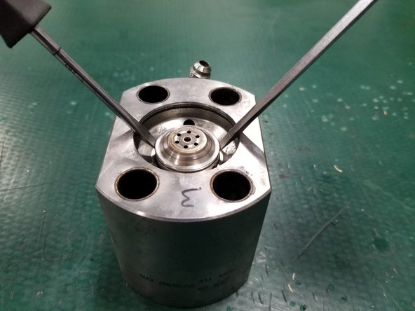 Carefully lift the check valve assembly using two flathead screwdrivers in the groove on the check valve body