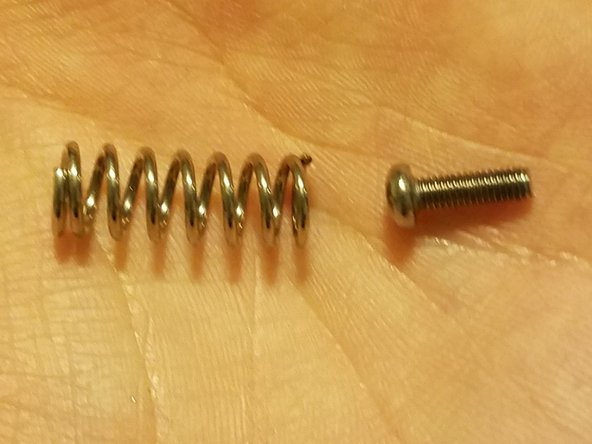 Place one of the hex screws you removed from the stock motor frame inside of the new spring, then compress it and slide it into position between the idler arm and frame.