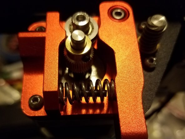 Place one of the hex screws you removed from the stock motor frame inside of the new spring, then compress it and slide it into position between the idler arm and frame.
