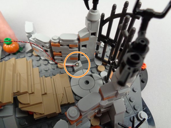 As shown by the orange circle in the first photo for this step, mount the first green LED light just inside the gate to Jack's house.