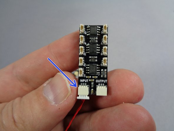 As shown by the blue arrow in the first photo for this step, connect the other end of the red cable from the TRUNK08 controller to the INPUT plug on one of the BRANCH09X adapters.