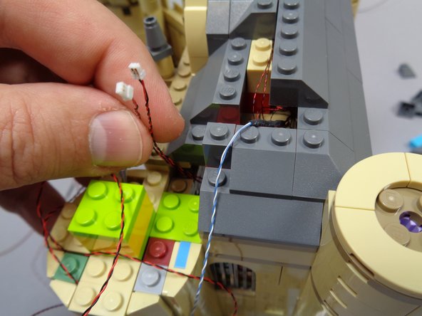 As shown in the second photo, pull the two light wires through the gap in the roof behind the tower.