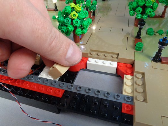 As shown in the photos for this step, temporarily lift the 2x3 tan brick and run the control cable between the studs on the black bottom plate, then re-attach the tan 2x3 brick on top of the control cable.