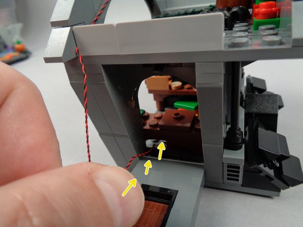As shown by the yellow arrows  in the first and second photos for this step, pass the LED light wire through the open wall, underneath Jack's desk and out the back side of the house.