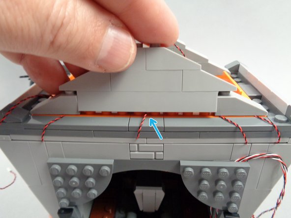 Finally, as shown by the blue arrow in the third photo for this step, route the light wire for the spotlight between studs in the center of the long orange plate, and re-attach the rest of the roof frame.