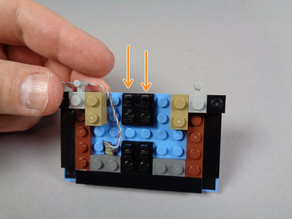 As shown by the two orange arrows in the first photo for this step, re-attach the two black plates with clips to the pre-lit marquee base.