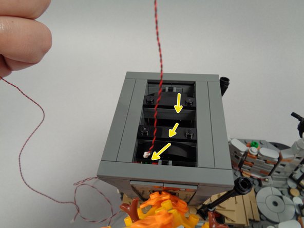As shown by the yellow arrows in the first photo for this step, pass the light wire for the yellow front door light down through the center of the house's first floor.