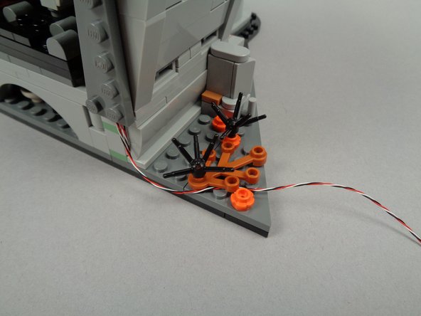 As shown by the two photos for this step, you can route the control wire to the edge of the town hall section base by passing it beneath the brown leaf and orange flower plate parts to hold it in place.
