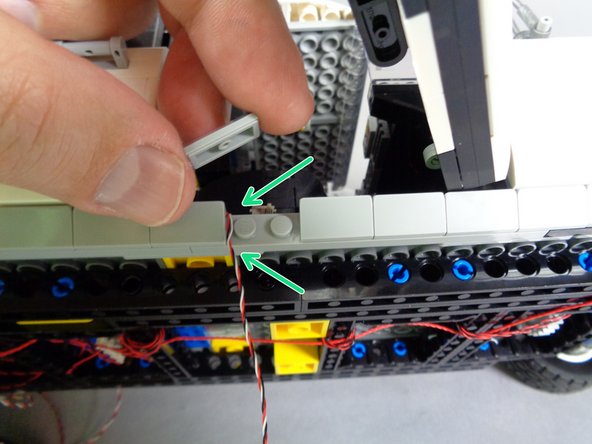 As shown by the green arrows in the second photo for this step, remove one of the 1x2 light bluish gray slopes from the frame and pass the wire down.  Make sure it passes between, not on top of, any studs.