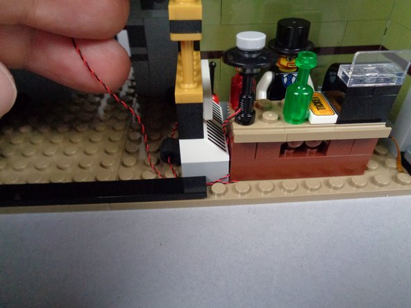 As shown in the third photo for this step, pass the lamp LED light wire back through the rubber Technic parts following the same path as the fireplace light wire.