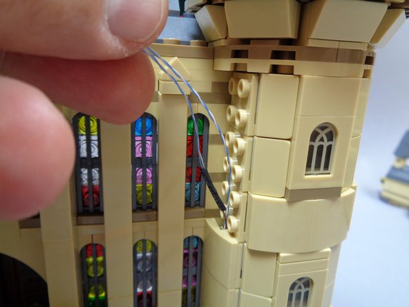 Continue re-attaching the tan slope pieces as you guide the wires for the two torches up the side of the castle tower as shown in the first and second photos.