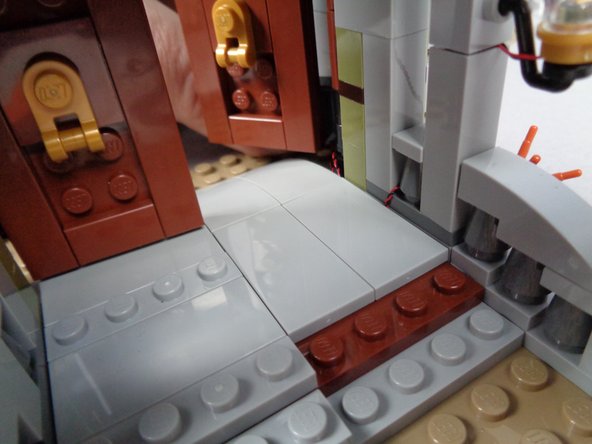 As shown in the first photo for this step, carefully replace the 2x4 LEGO tile on the porch floor, making sure the light wire continues as close to the wall as possible so as not to be pinched passing on top of any studs.