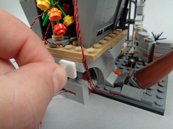 As shown in the photos for this step, take one of the large sticky squares included with your light kit and attach it to the back of Jack's house in the position shown in the second photo.