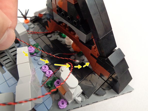 As shown by the yellow arrows in the first photo for this step, pass the yellow LED light wire under the gap in the wave.