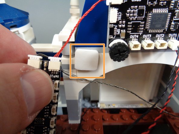 As shown by the orange square in the second photo, attach a large sticky square to the back castle wall area to the left of the TRUNK08 master controller.