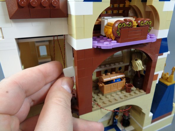 As shown in the first photo for this step, use a large sticky square to hold the light wire on the magic room ceiling behind the brown pillar.