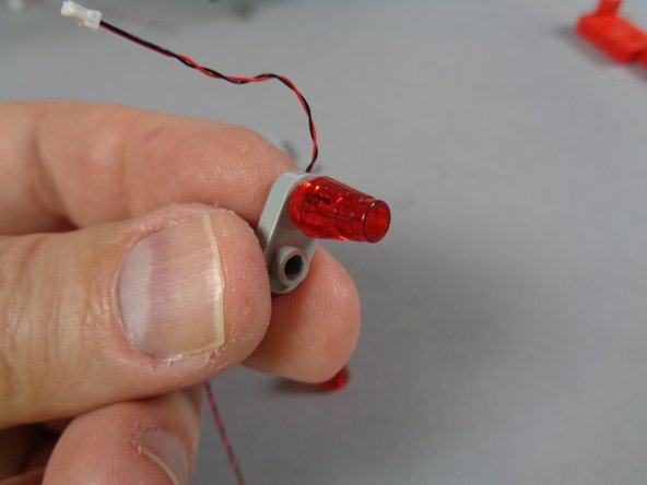 As shown in the third photo for this step, re-attach one of the transparent red cones on top of the LED light.