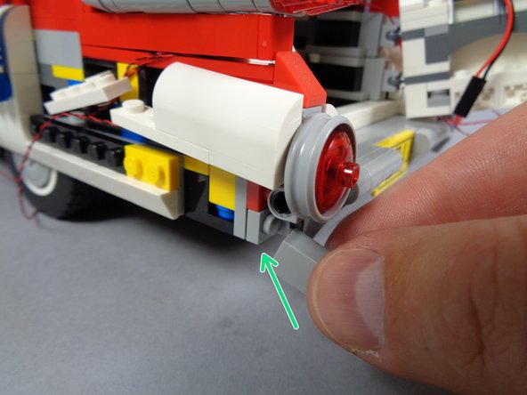As shown by the green arrow in the first photo for this step, re-attach the brick below the round tail light frame.