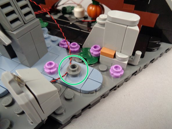 The green circle in the second photo shows a 1x1 round plate mounted to raise the R.I.P. tombstone a little to allow the LED light wire to pass underneath.  This plate was taken from the spare LEGO parts from the original set-- this part is not included with your light kit.  You can use any 1x1 piece from your own spare set parts.