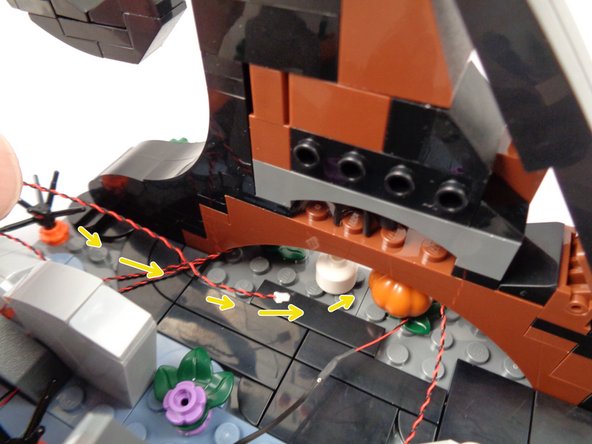 As shown by the yellow arrows in the first photo for this step, pass the LED light wire back and under the wave frame.