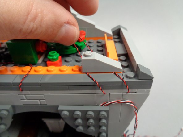 As shown in the second photo for this step, re-attach the rightmost lower roof frame slope to hold the two wires in place.