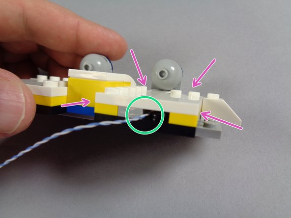 As shown by the green arrow in the second photo, re-attach the light bluish gray plate behind the blue light, again being careful to make sure the LED light wire runs to the side of the plate.