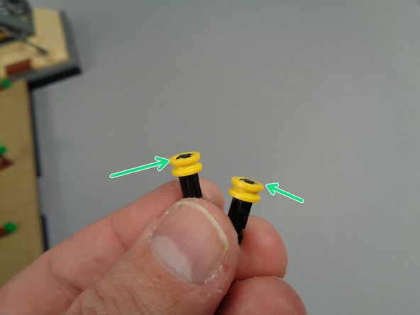 As shown in the second and third photos for this step, prepare the two short black axle parts by attaching one round bushing piece to the top of each axle.