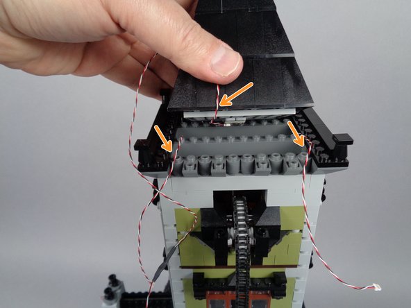 Carefully re-attach the top roof section.  As shown by the three orange arrows in the second photo for this step, make sure the three wires pass out the back of the tower between studs, not on top of any studs.
