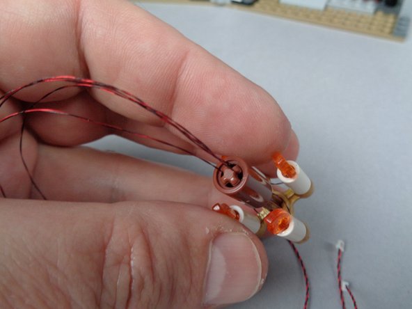 As shown in the second photo for this step, carefully slide the brown LEGO connector part over the center axle of the chandelier, making sure to keep gentle pressure on the wires so they stay straight as you lower the connector part.