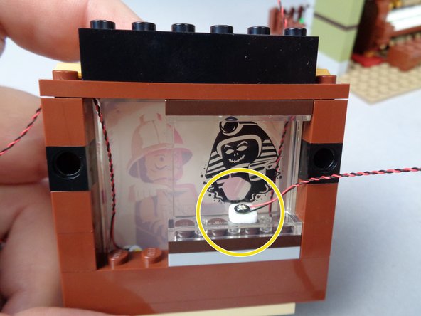 As shown by the yellow circle in the second photo for this step, attach the red LED light to the back of the Sphinx frame, in the center of the frame so it points upward toward the Sphinx as shown.