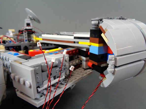 As shown by the blue dotted lines and circle in the third photo, feed the four cockpit control panel wires through a hole in the Technic brick in the Falcon frame, and into the open space near the &quot;engines&quot; speaker.