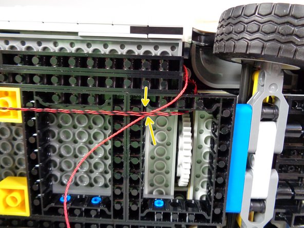 As shown by the green arrows in the first photo for this step, pass the two strobe light wires through the hole in the black Technic frame, and pull toward the back of the Ecto-1.