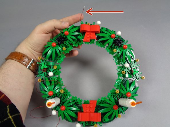 As shown in the photo for this step, when you are finished running the wire for the first candle, the plug should reach the top center of the wreath, at the bow.