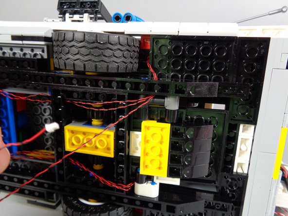 As shown in the second and third photos for this step, continue passing the wire along the same path as the other two, opening the ramp to allow the wire to pass behind the ramp bracket.