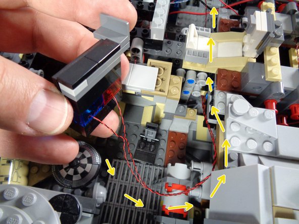 As shown by the yellow arrows in the first photo for this step, pass the two LED light wires behind the computer and toward the center of the Falcon.