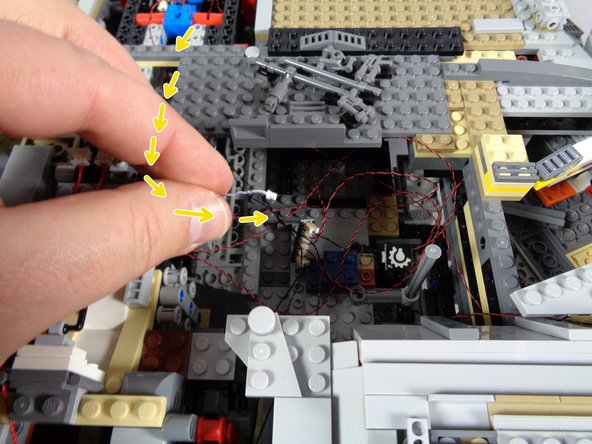 As shown by the yellow arrows in the first photo, carefully run the other end of the wire you just connected (the end with the small plug) through the interior Falcon frame, back to the same area as the four cockpit control panel light wires.