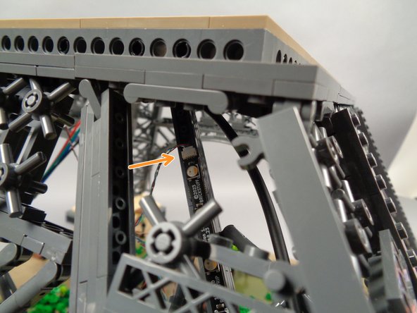 As shown by the orange arrow in the second photo, carefully pass the light strip connected to plug #1 on the adapter board down through the top of the first pillar with its connecting plug at the top of the pillar.