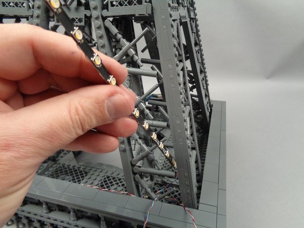 As shown in the first photo for this step, peel the backs off of the sticky squares on the fourth pair of light strips, and pass the strip connected to plug #1 on the adapter board into the center of the pillar.