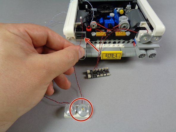 As shown by the red circle and red arrow in the first photo for this step, pass the light wire for the headlight on the RIGHT of the second assembly through the dark bluish gray bracket.