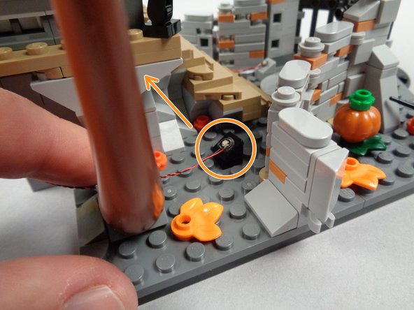 As shown by the orange circle and arrow in the first photo for this step, mount the second green LED light just in front of the tree next to Jack's house, and position the LED light so it shines up toward the tree.