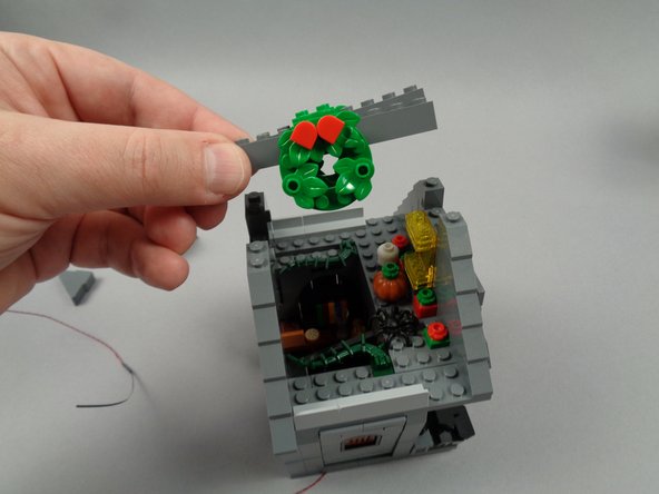 As shown in the photos for this step, remove the front and back roof slope sections above the cross-beam (the part with the wreaths), then remove the two cross-beam sections as well.