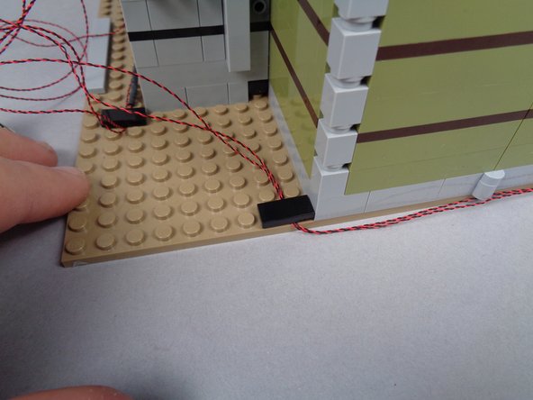 As shown by the purple rectangle in the second photo for this step, carefully bend the wires around the back side of the mansion, making sure the wires run between, not on top of, any studs.