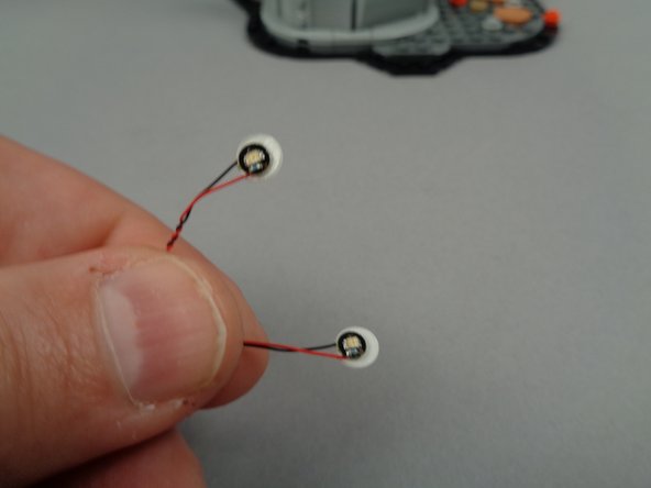 As shown in the third photo for this step, attach sticky dots to the back of both green LED lights.