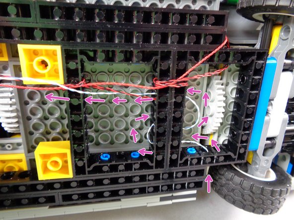 As shown by the green circle and green rectangles in the second photo for this step, feed the hood spot light wire through the holes in the side and center black Technic frames several times to pull it tight.