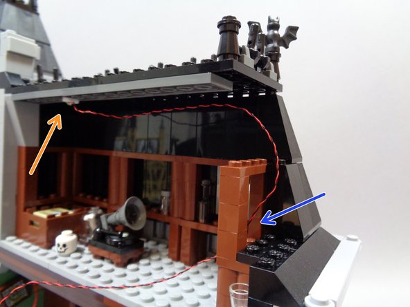 As shown by the orange arrow in the second photo, mount the orange Pico LED light on the attic ceiling and route the wire around and through the gap in the brown parts as shown by the blue arrow.