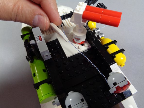 As shown in the second photo for this step, remove the white 2x4 tile from the roof.  This will expose the black plate below, which has holes through which you will pass the LED light wires.