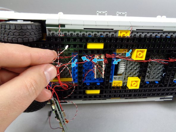 As shown by the blue arrows in the second photo for this step, pass the door switch wire through the holes in the black Technic frame so it passes back toward the main controller.