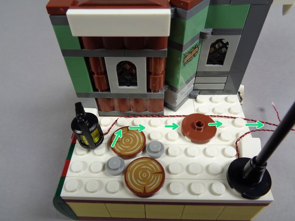 As shown in the first photo, re-attach the lantern to the white base, making sure its wires run up against the house and toward the back as shown by the green arrows.