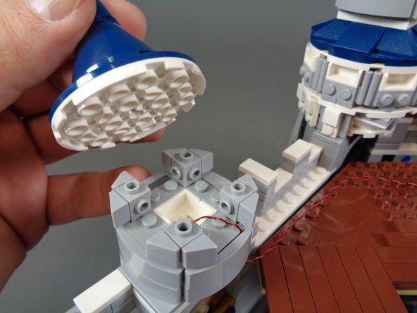 As shown in the photos for this step, carefully re-assemble the first tower, making sure the LED light wire runs between, not on top of, any studs.